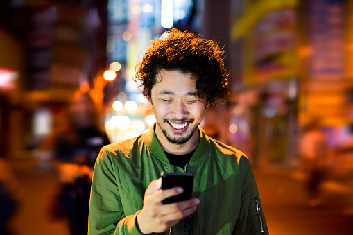 Happy japanese young man with smart phone at night, Tokyo.