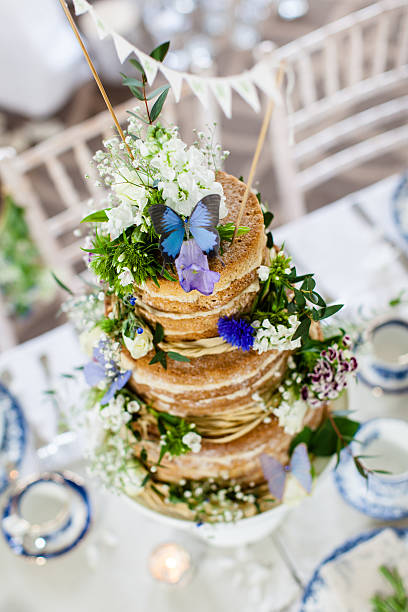 Naked wedding cake with edible flowers on a wedding table decorated with wild flowers and vintage plates and tea cups