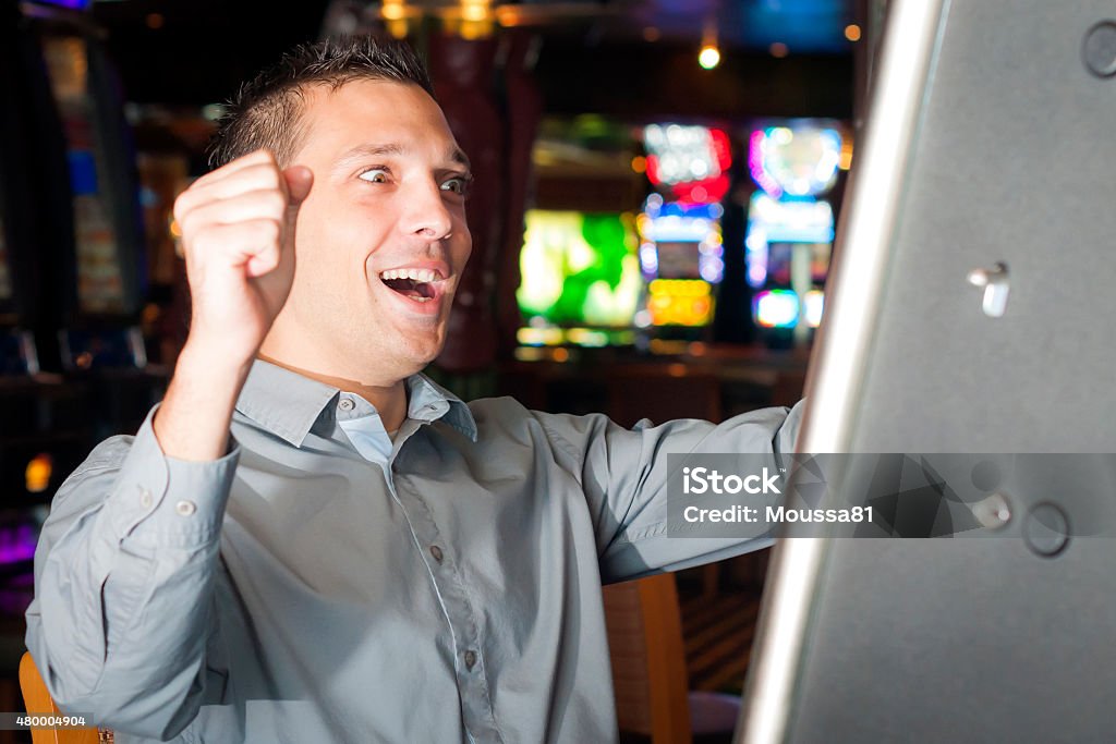 Young man playing a slot machine Young man in his 20s wearing hair gel and a grey shirt is playing a slot machine 20-29 Years Stock Photo