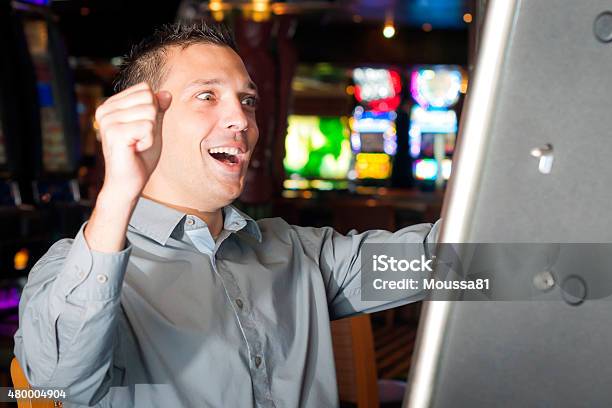 Young Man Playing A Slot Machine Stock Photo - Download Image Now - 20-29 Years, 2015, Addiction