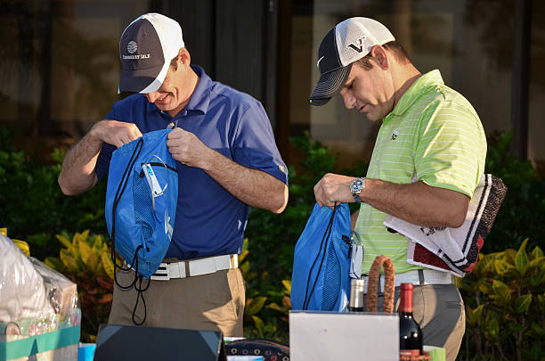 Two men at a golf charity event with goody bags Palm Beach Gardens, FL, USA - May 18, 2013: Two men dressed in golf attire standing behind a table of gifts at a charity golf event benefiting juvenile diabetes. They are looking into their goody bags.  gift lounge stock pictures, royalty-free photos & images