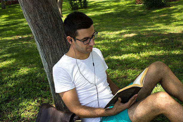 istock Side view of young man reading book in a park 480013258