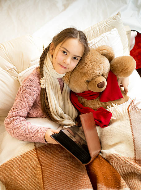 istock cute girl reading book to teddy bear at bed 480022150