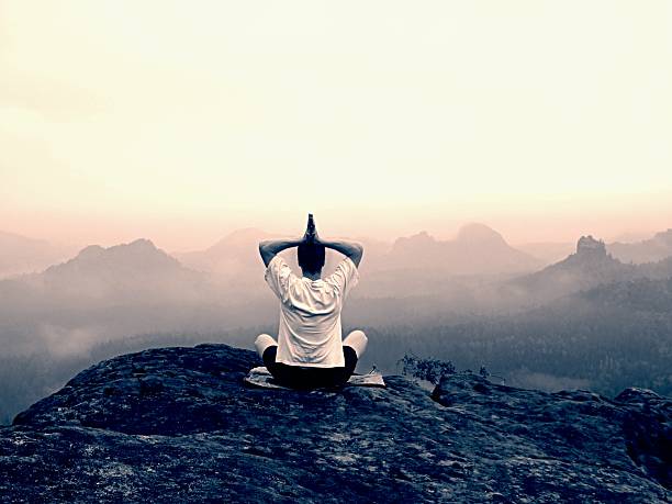 istock Man do Yoga pose on rocks peak within misty morning 480025662