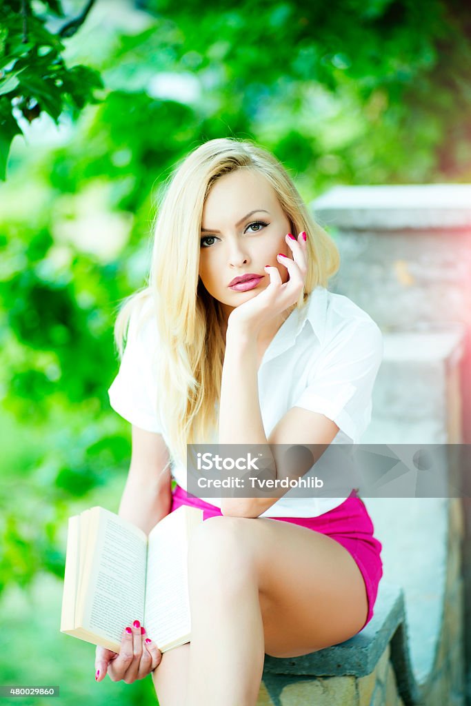 Pretty girl with book Attractive pretty blond girl sitting outdoor with book in summer on green natural background, vertical picture 2015 Stock Photo