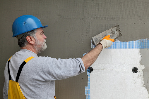 Worker spreading  mortar over styrofoam insulation and mesh  with trowel