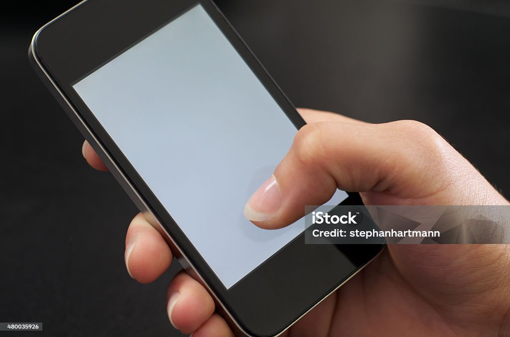 Woman holds mobile phone in one hand - Woman holding cellphone A woman's hand holds a mobile phone against a black background. The screen is white with no content. The right thumb touches the screen at the bottom. Scrolling Stock Photo