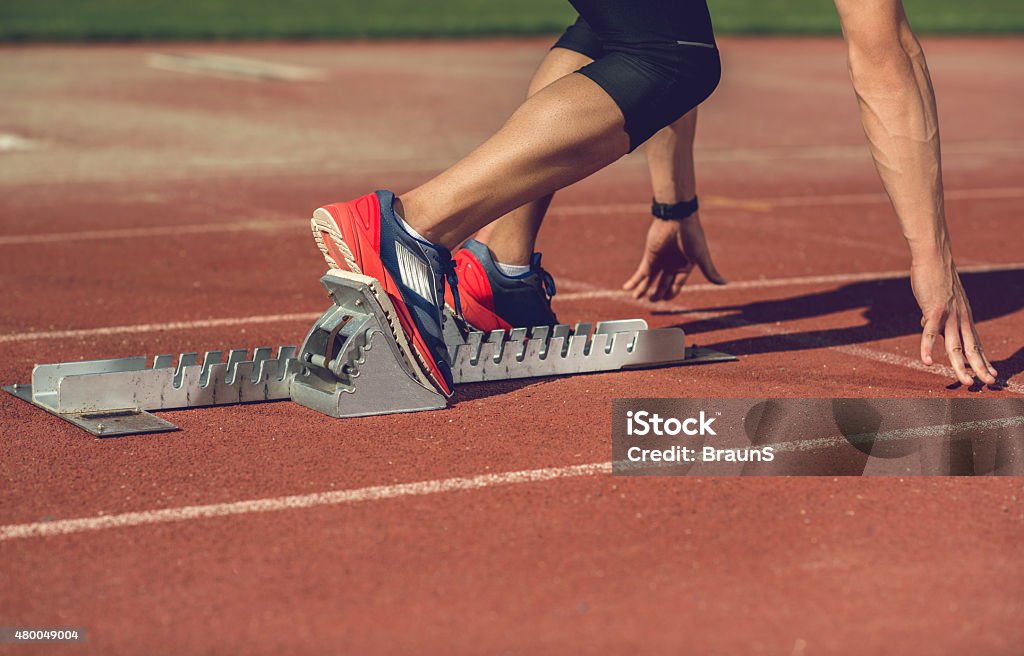 Unrecognizable man preparing to start a race on running track. Unrecognizable athlete on a starting line at running track. Track Starting Block Stock Photo