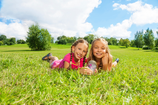 Two happy little nine years old girls hold jar with butterfly laying in the grass and showing big smile on happy faces