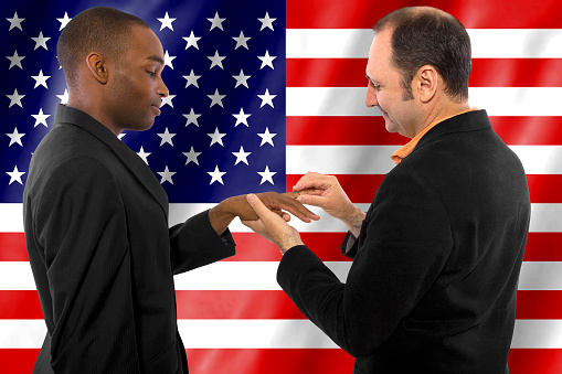 Photo of same sex gay couple legally married in United States of America.  The background is an American flag.  The image is a celebration of the legalization on gay marriage.  This depicts human and civil rights and equality in the United States.