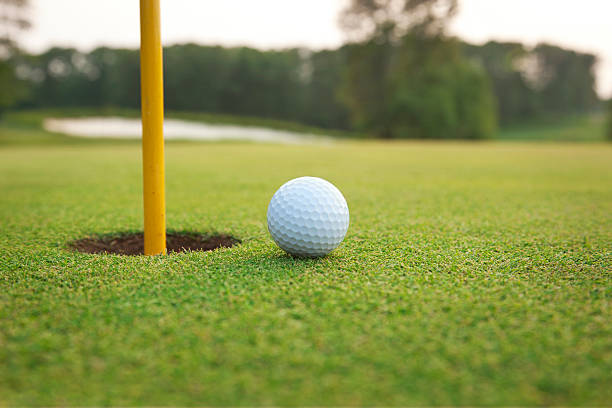 nahaufnahme des golfball auf einem grünen in der nähe von loch - golf golf flag sunset flag stock-fotos und bilder