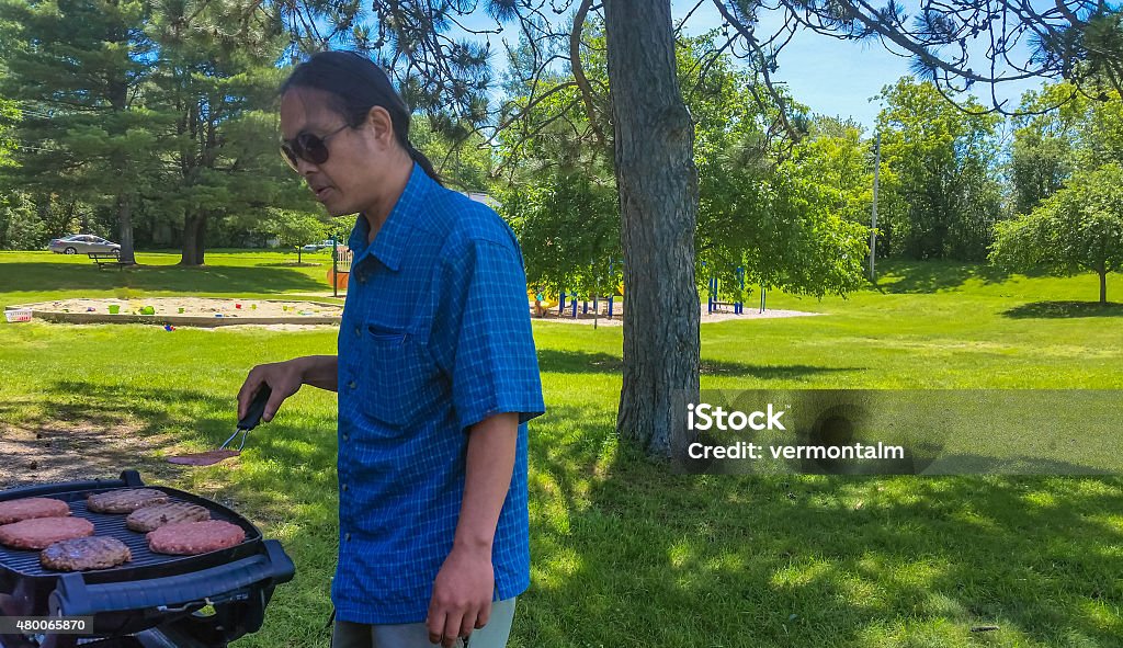 the grillmaster Asian man enjoying grilling hamburgers for a picnic in the park  2015 Stock Photo