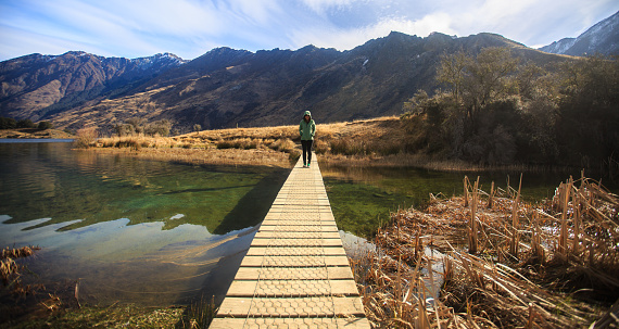 Young adult woman standing alone on the bridge at Moke Lake, Queenstown, New Zealand