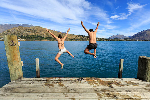 Young couple jumping to the lake Young couple jumping on the edge of a dock into the Lake Wakatipu jumping into water stock pictures, royalty-free photos & images