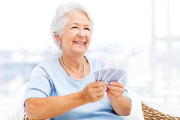senior woman playing cards mientras mirando a - bridge juego de cartas fotografías e imágenes de stock