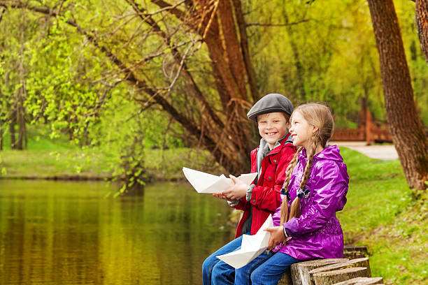 sorridente menina e menino sentar-se perto de nice lago jogar - ticket ticket stub park fun imagens e fotografias de stock
