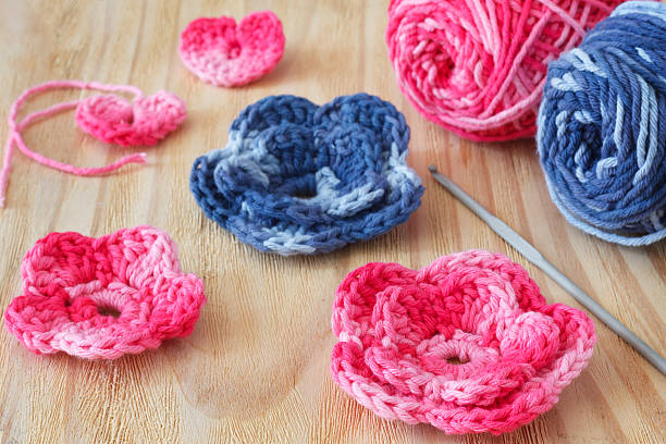 Handmade pink and blue crochet flowers and heart Handmade pink and blue crochet flowers and heart with skein on wooden table. Selective focus clew bay stock pictures, royalty-free photos & images