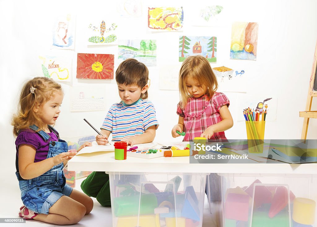 Three creative kids Kindergarten kids by the table gluing and painting on creative art class Child Stock Photo