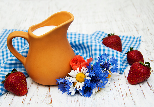 Jug of milk, strawberries and wildflowers on a old wooden background
