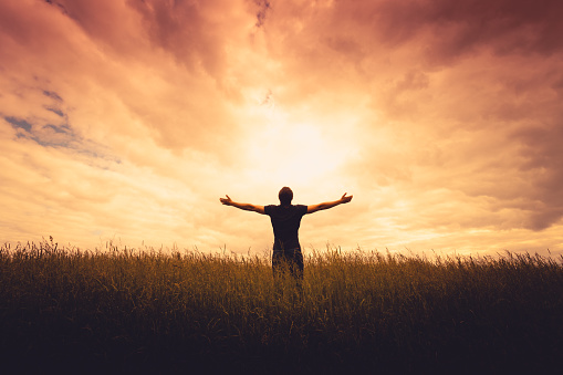 silhouette of man standing in a field at sunset