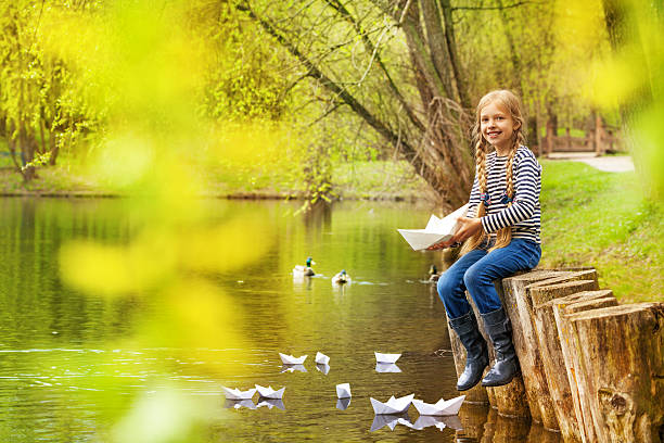 menina perto de lago jogando com barcos de papel na floresta - ticket ticket stub park fun imagens e fotografias de stock