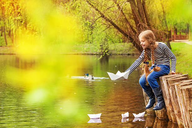 menina sentada perto de lago jogando com barcos de papel - ticket ticket stub park fun imagens e fotografias de stock