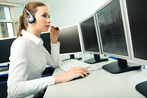 Photo of pretty consultant wearing headset and sitting in front of computer display while consulting client   Note to inspector: the image is pre-Sept 1 2009