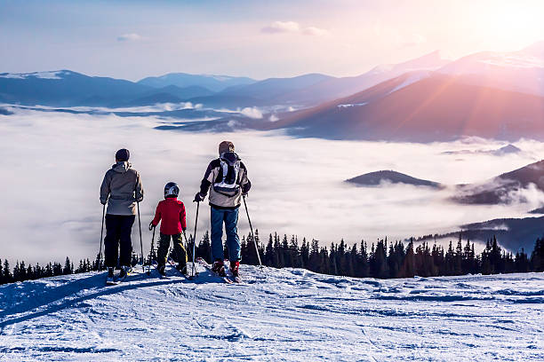 People observing mountain scenery Family of three people stays in front of scenic landscape. These are skiers, they dressed in winter sport jackets and have skies attached top of ski mountain stock pictures, royalty-free photos & images