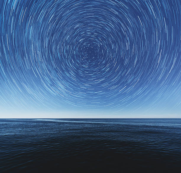Infinite View The ocean stretches to the horizon under a canopy of spinning stars. Earth's axis is revealed at the center. Composite image. never ending photos stock pictures, royalty-free photos & images