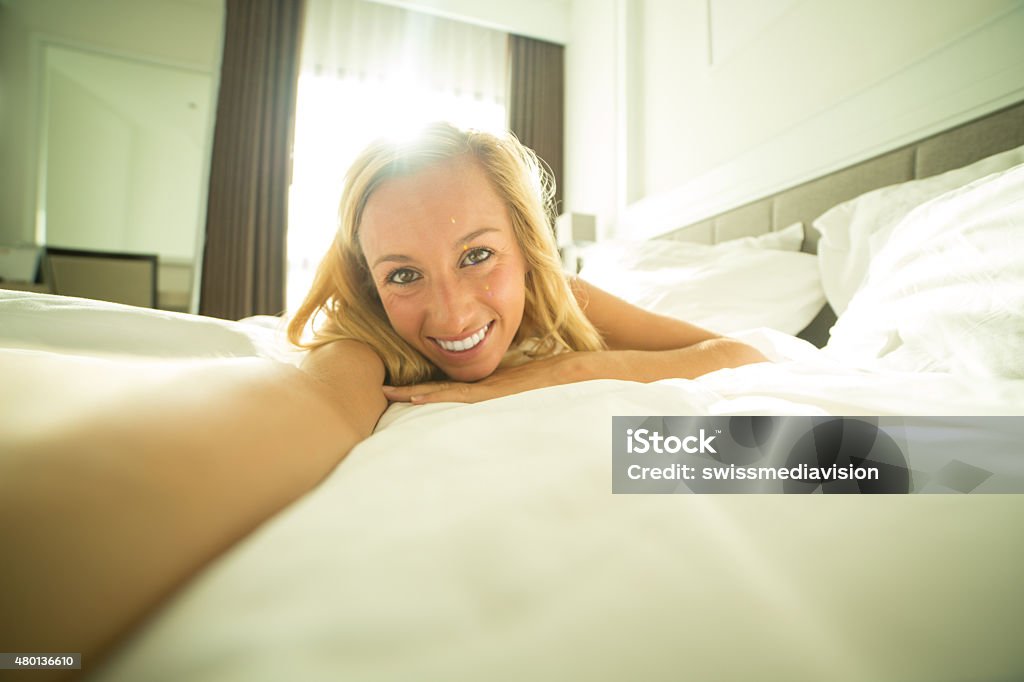 Morning selfie of woman waking up Young funny woman on a bed in an hotel room taking a selfie in the morning. Sunlight coming in the room. 2015 Stock Photo