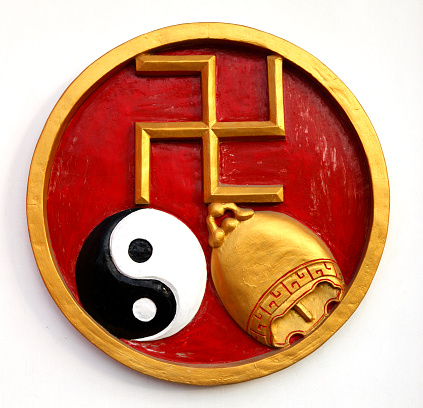 A wall decoration in Bali, with a golden swastika, a ying yang and a golden bell. This is a religious symbol of good luck.