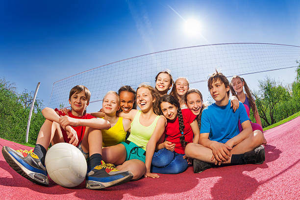Happy teenagers who sit on volleyball game court Happy teenagers who sit on volleyball game court holding ball during summer sunny day young volleyball girl stock pictures, royalty-free photos & images