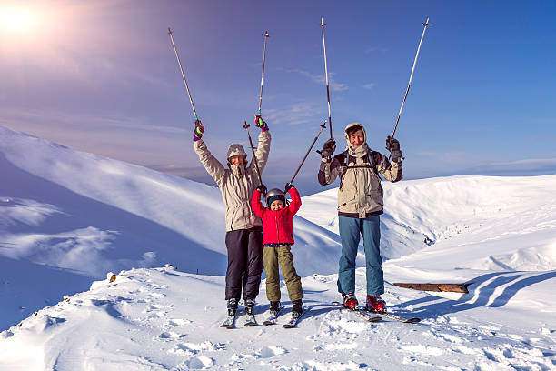 Winter sport family enjoy traveling together Family of three people - parents and little daughter - on winter mountains background happy laughing faces victory raised hands with ski poles top of ski mountain stock pictures, royalty-free photos & images