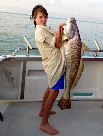 Twelve year old boy struggles to hold a big jew fish that he caught.