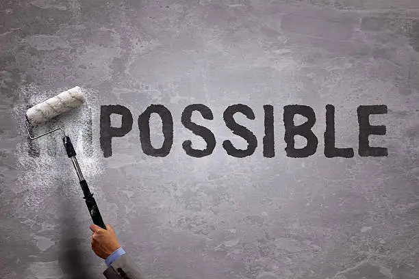Changing the word impossible to possible by painting over and erasing part of the word with a paint roller on a concrete wall