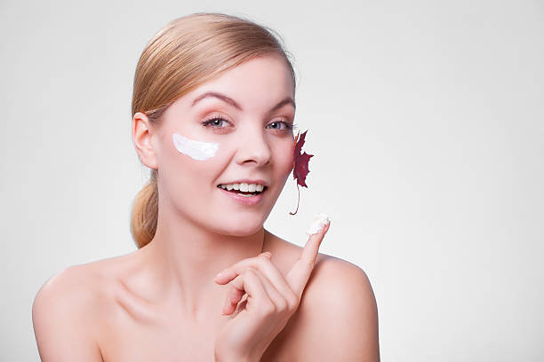 Skin care. Face of young woman girl with maple leaf. Skincare habits. Face of young woman with leaf as symbol of red capillary skin on gray. Girl taking care of her dry complexion applying moisturizing cream. Beauty treatment. regenerative face cream stock pictures, royalty-free photos & images