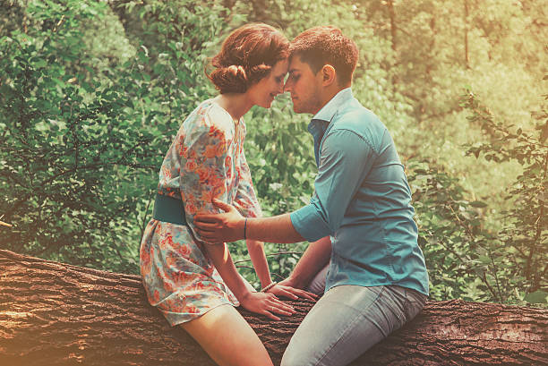 Young couple in love sitting on fallen trunk tree in summer park, tender scene. Image with sunlight effect