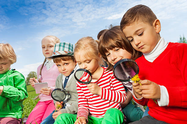 istock Group of children sitting in field with magnifier 480154524