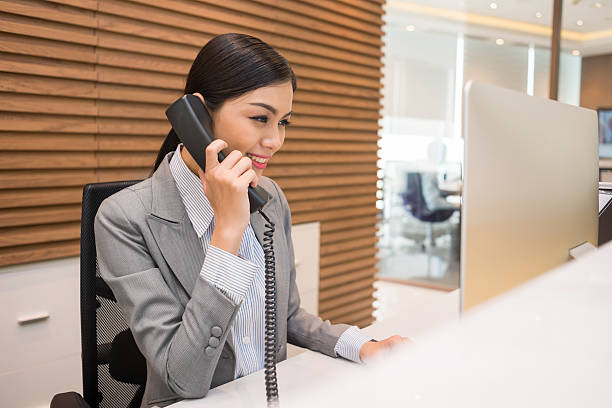 Pretty Vietnamese receptionist Pretty Vietnamese receptionist talking on telephone at her workplace receptionist stock pictures, royalty-free photos & images