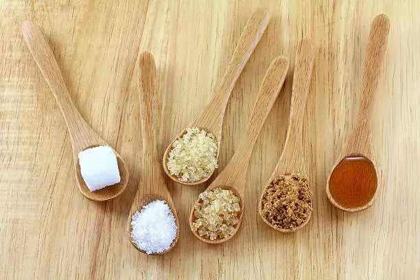 Spoons of different types of sugar on the wooden background