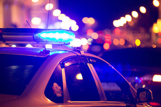 Emergency vehicle lighting Blue light flasher atop of a police car. City lights on the background.  police officer stock pictures, royalty-free photos & images