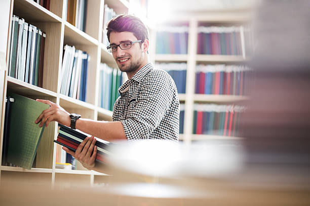 istock Happy young man taking books in a library. 480175698