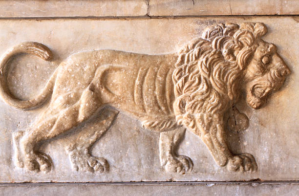 An ancient bas-relief of a marble lion roars on exterior wall, Rome, Italy. The stone is a tawny brown; the lion is walking.