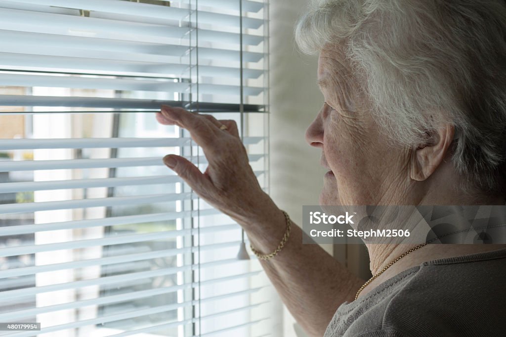 Senior femme regardant par la fenêtre à volets - Photo de Voisin libre de droits