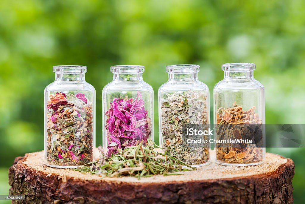 Bottles with healing herbs on wooden stump Glass bottles with healing herbs on wooden stump on green background, herbal medicine. 2015 Stock Photo