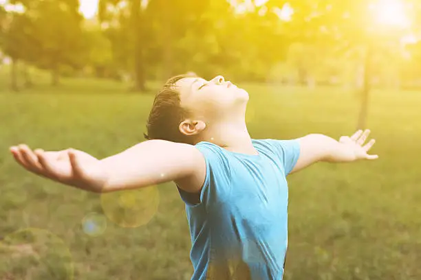 Young boy standing in sun light with his arms outstretched