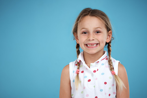 Caucasian little girl with blue backpack with a toothy smile is looking at camera in front of white background.