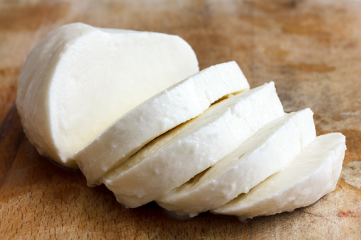 Single ball of mozzarella cheese sliced and isolated on rustice wood.