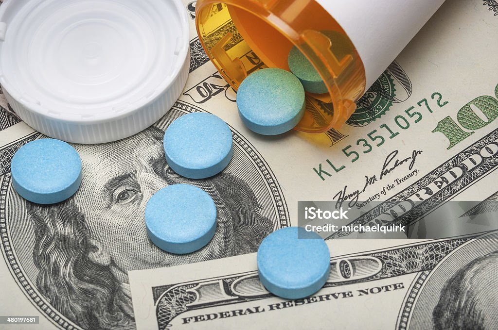 Prescription medicine and money Pills spilling out of a prescription bottle on 100 dollar paper currency Prescription Medicine Stock Photo