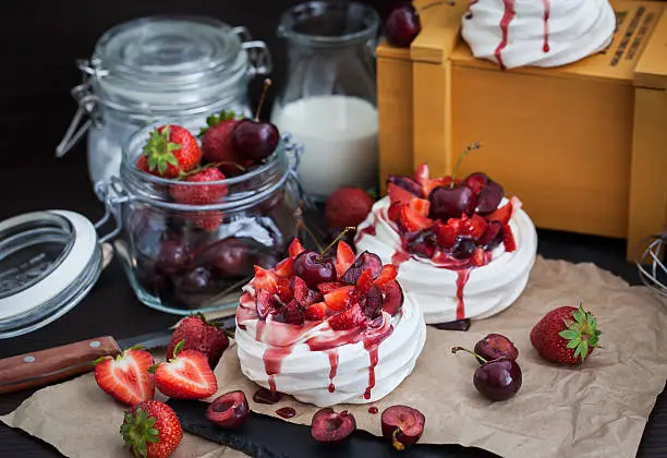 Portion of mini Pavlova meringue cake decorated with fresh strawberry and cherry
